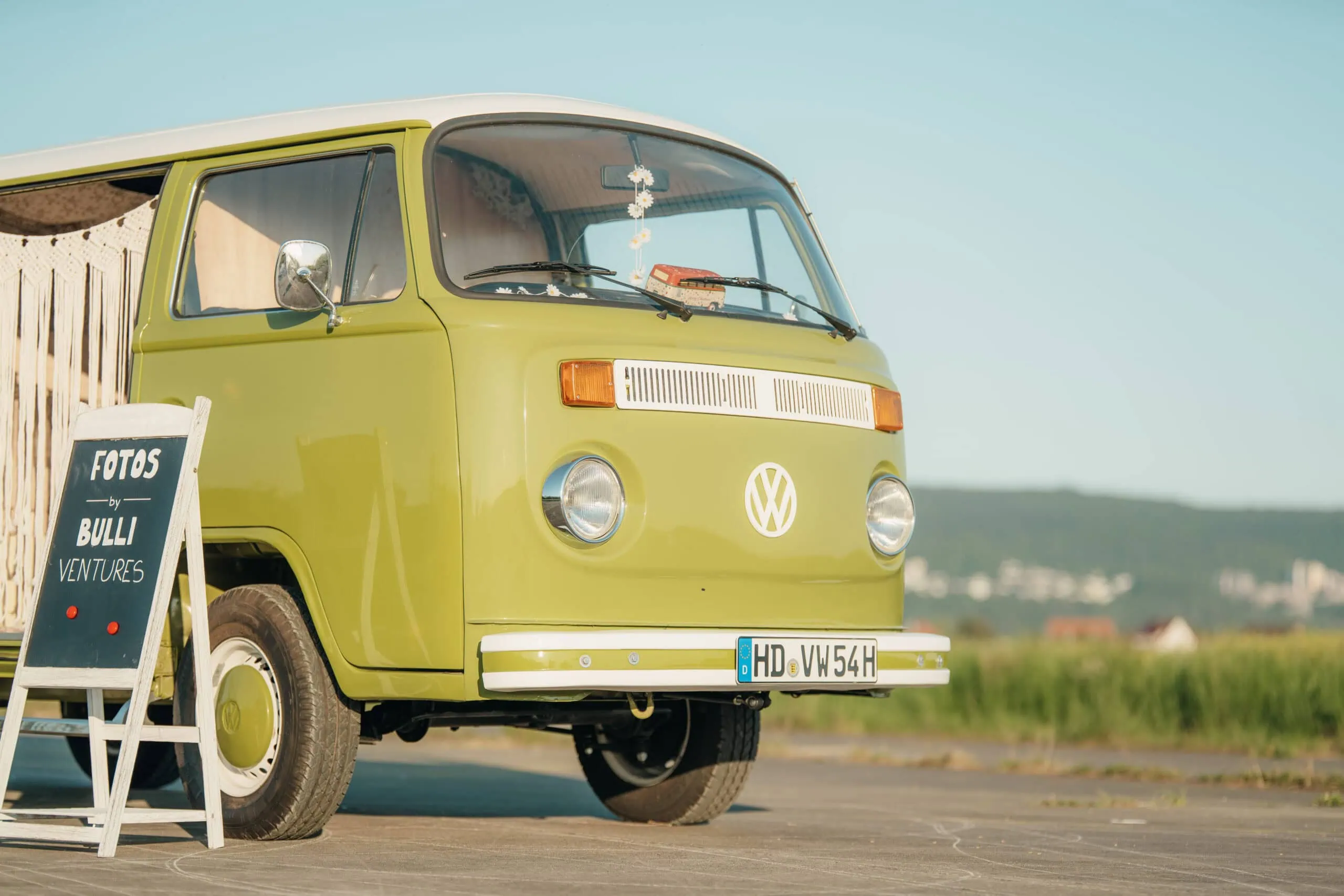 Grüner Oldtimer-Fotobus Martha neben einem Schild mit der Aufschrift FOTOS BULLI VENTURES.