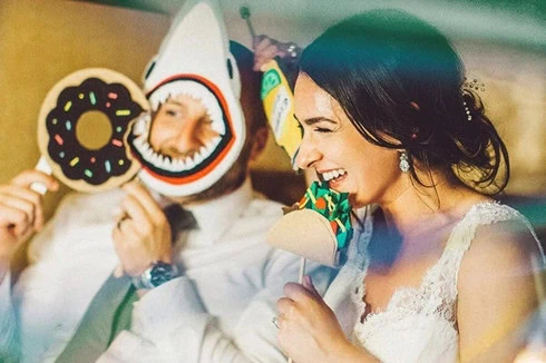 Braut und Bräutigam halten bei ihrer Hochzeit verspielte Masken vor dem Fotobulli hoch.