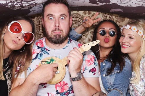 Vier Erwachsene posieren verspielt im Fotobus - ein Mann mit kleiner Gitarre, drei Frauen mit Sonnenbrillen.