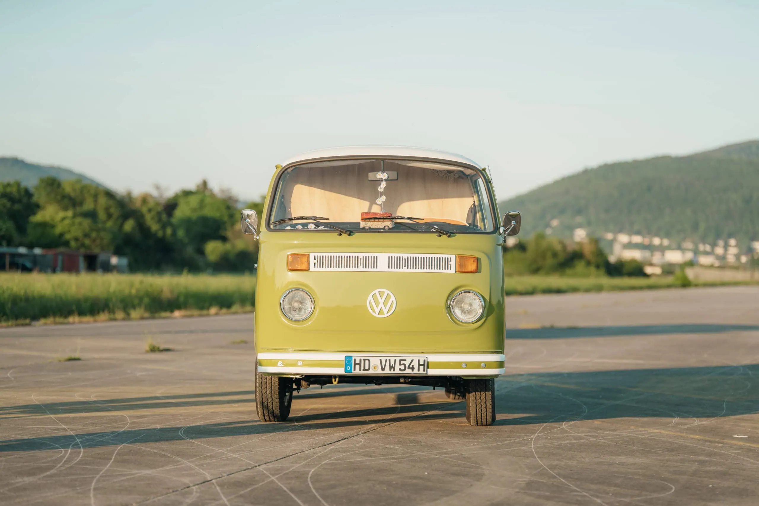 Fotobus Martha: grün-weißer VW T2 Oldtimer-Bulli auf gepflasterter Fläche, im Hintergrund Gras und Hügel.